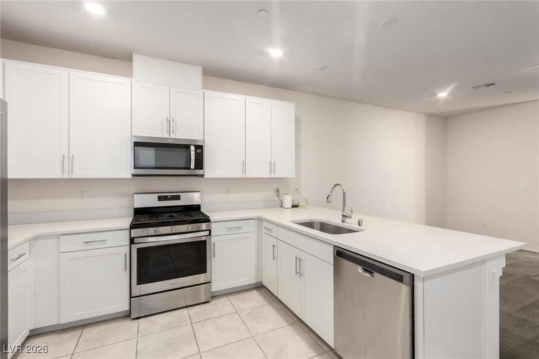 2862 Turnstone Ridge Street Henderson, NV 89044 - Photo 12 of 30 Kitchen featuring appliances with stainless steel finishes, recessed lighting, a peninsula, white cabinetry, and light stone countertops