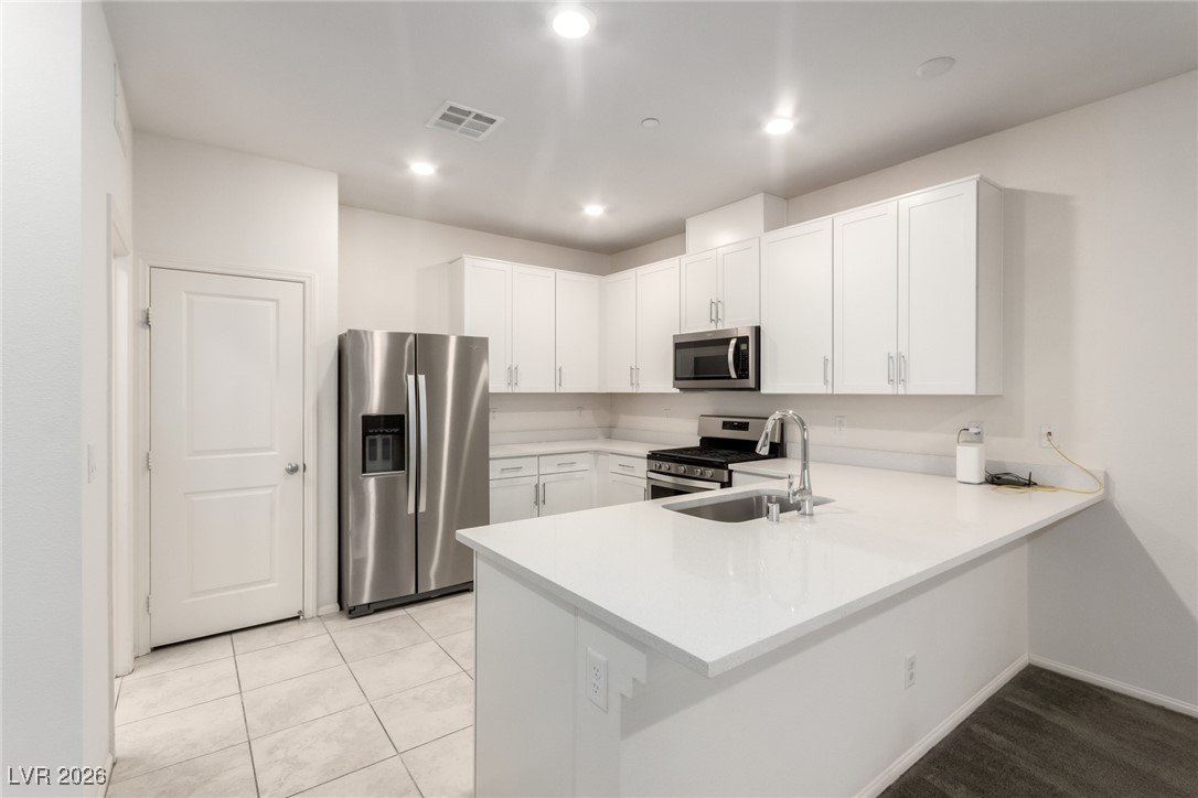 2862 Turnstone Ridge Street Henderson, NV 89044 - Photo 2 of 30 Kitchen featuring stainless steel appliances, white cabinetry, a peninsula, light tile patterned floors, and light stone counters