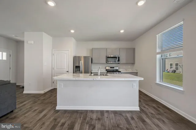 a view living room with stainless steel appliances granite countertop a sink a microwave a refrigerator a microwave oven and white cabinets with wooden floor