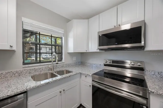 a kitchen with granite countertop white cabinets appliances and a window