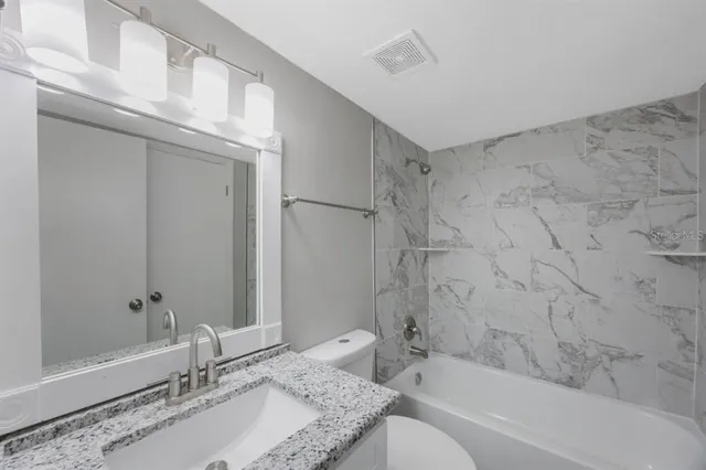 a bathroom with a granite countertop bathtub shower sink vanity and toilet