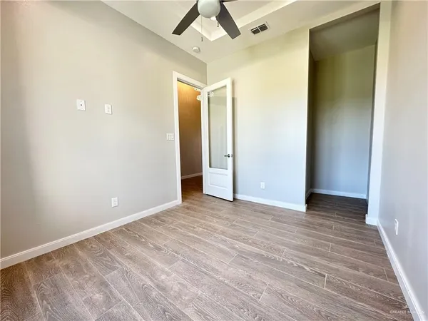 a view of an empty room with wooden floor and a ceiling fan
