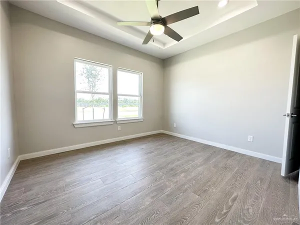 an empty room with wooden floor ceiling fan and windows