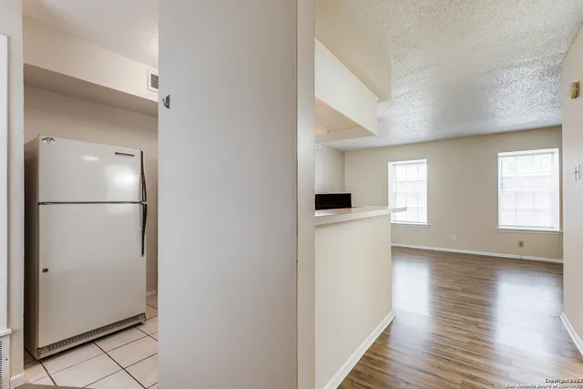 a view of an empty room with wooden floor and a kitchen