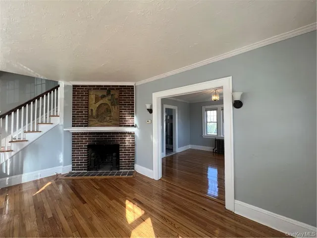 a view of an empty room with wooden floor fireplace and a window