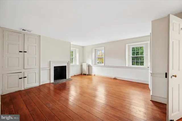 an empty room with wooden floor fireplace and windows