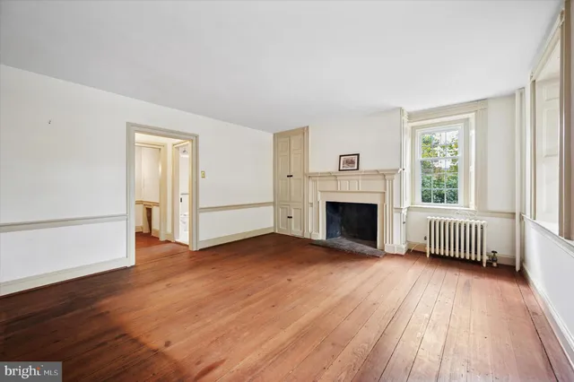 an empty room with wooden floor fireplace and windows