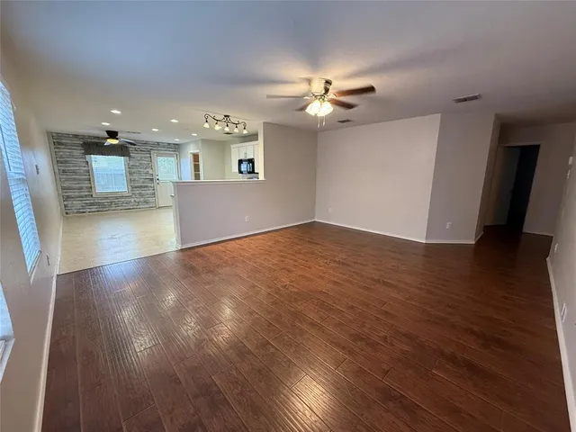 a view of an empty room with wooden floor and a ceiling fan