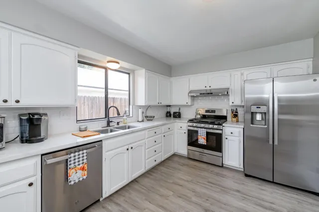 a kitchen with stainless steel appliances granite countertop a sink a stove a refrigerator and white cabinets