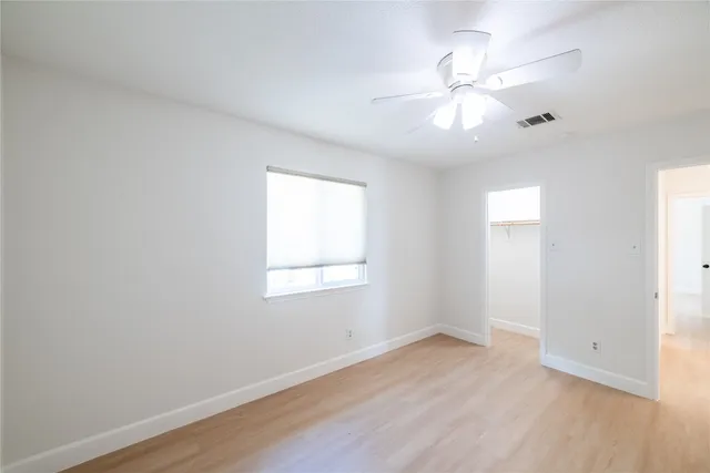 an empty room with wooden floor fan and windows