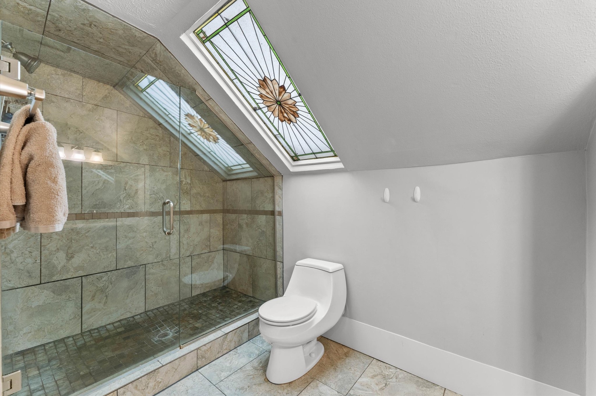 945 Harvard Street Houston, TX 77008 - Photo 21 of 47 Indulge in relaxation with this upstairs bathroom, featuring a luxurious spa tub and a sleek, glass-enclosed shower beneath a stunning stained glass skylight.