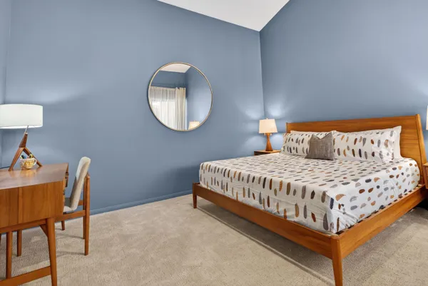 a bedroom with a bed a mirror and a lamp on dresser
