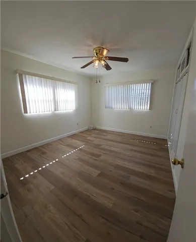 an empty room with wooden floor fan and windows