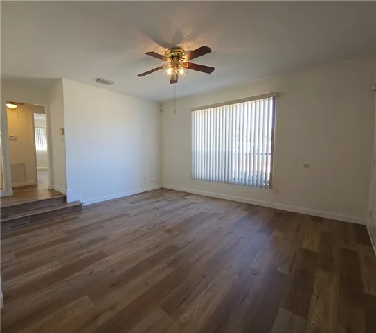 an empty room with wooden floor fan and windows