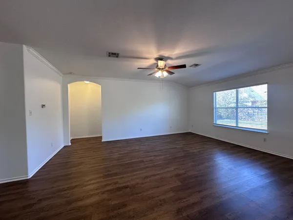 an empty room with wooden floor chandelier fan and windows
