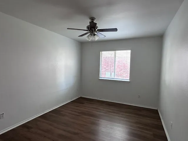 an empty room with wooden floor chandelier fan and windows