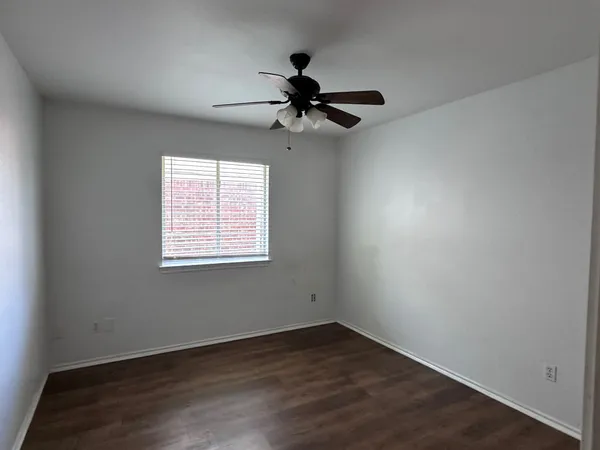 an empty room with wooden floor chandelier fan and windows