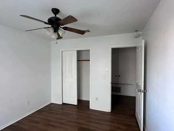 a view of an empty room with wooden floor and a ceiling fan