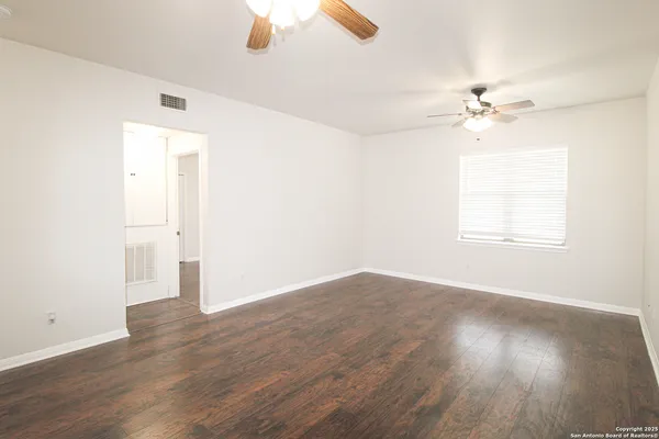 an empty room with wooden floor ceiling fan and window