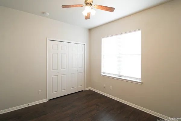 an empty room with wooden floor chandelier fan and windows