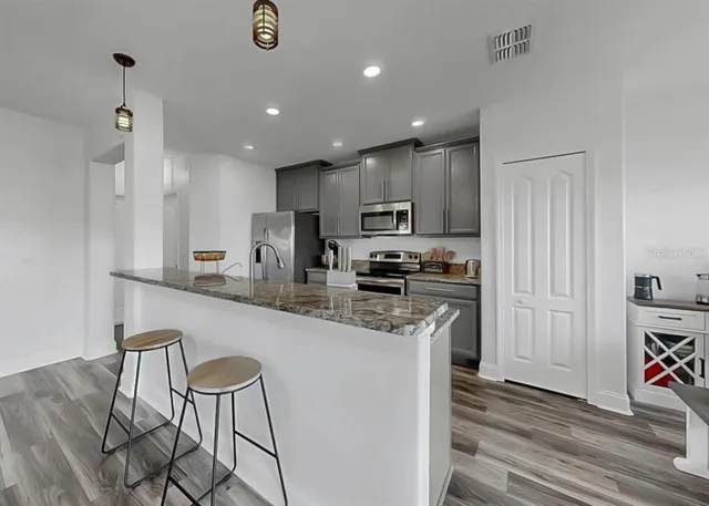 a kitchen with stainless steel appliances granite countertop a sink a stove a refrigerator cabinets and a dining table