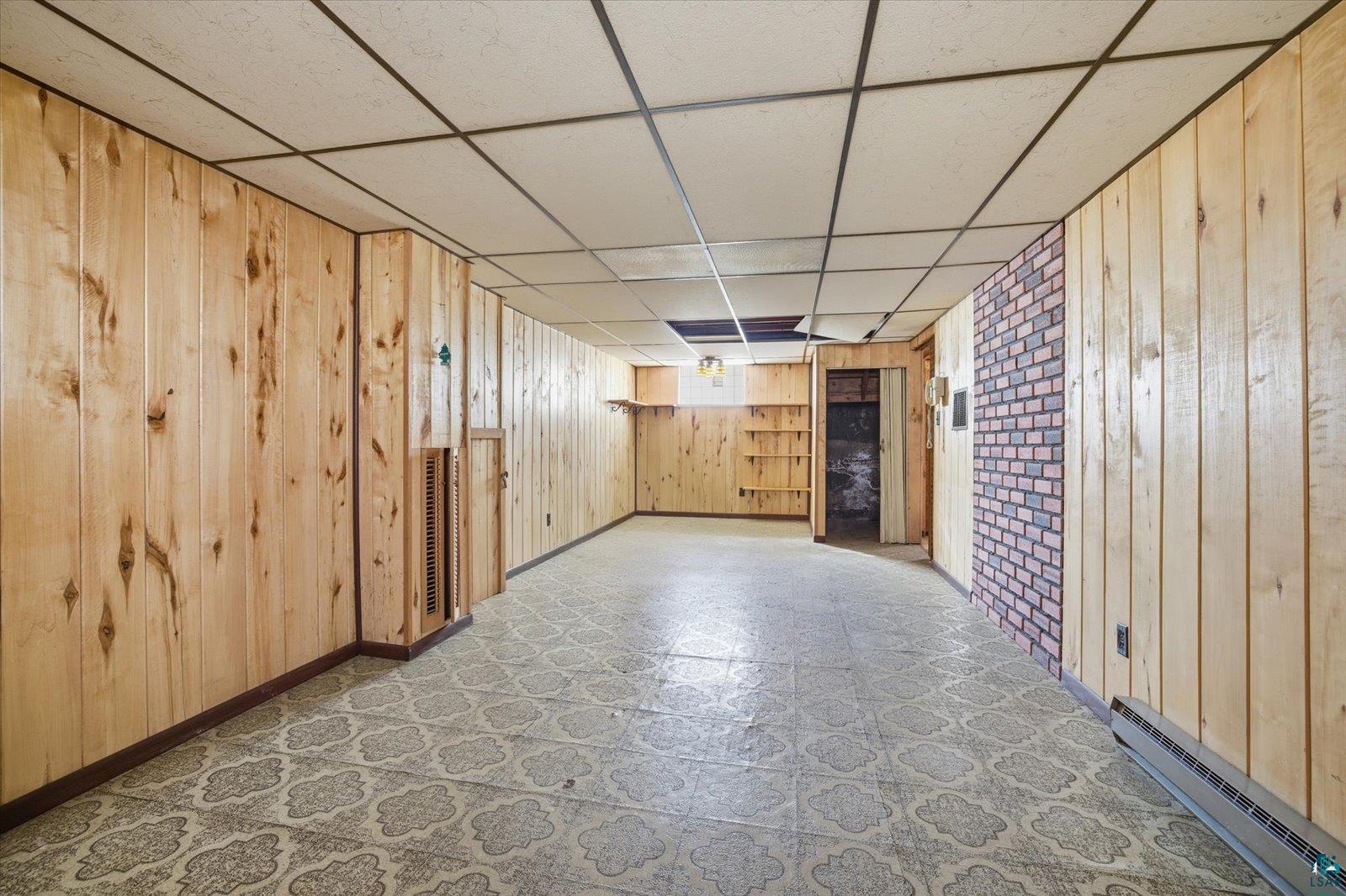 709 Michigan Street Hibbing, MN 55746 - Photo 19 of 47 Finished below grade area with a paneled ceiling, wood walls, a baseboard radiator, and tile patterned floors