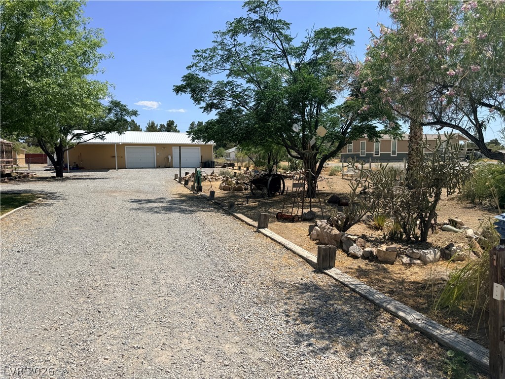 1391 West Dyer Road Pahrump, NV 89048 - Photo 7 of 50 A spacious gravel driveway leads to a three-bay garage and a verdant desert landscape.