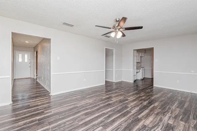 a view of an empty room with wooden floor and a ceiling fan