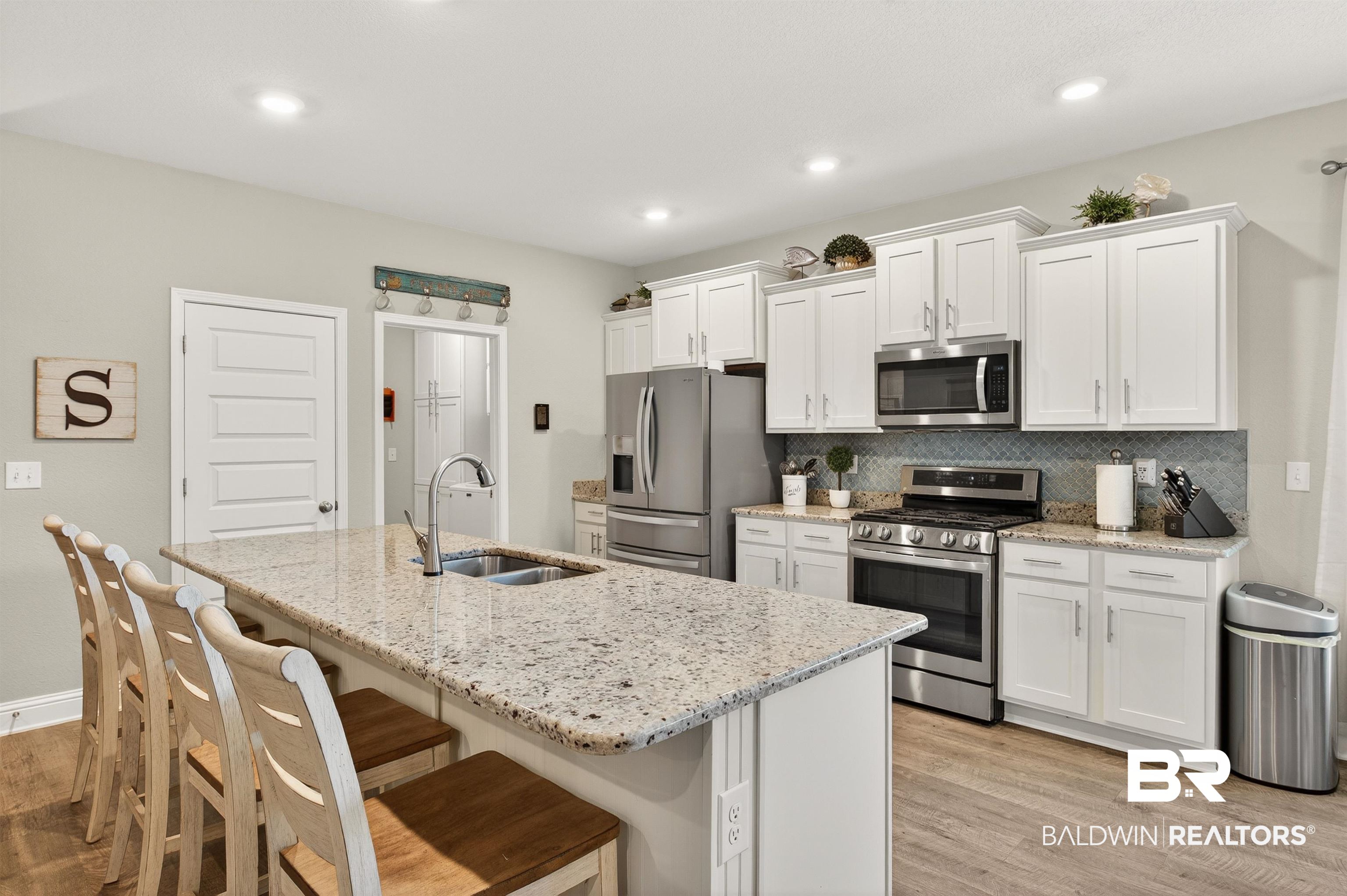 8735 Bronze Lane Foley, AL 36535 - Photo 8 of 58 Kitchen featuring a large central island with seating, light-toned countertops, white cabinetry, stainless steel appliances, and wood-finish flooring