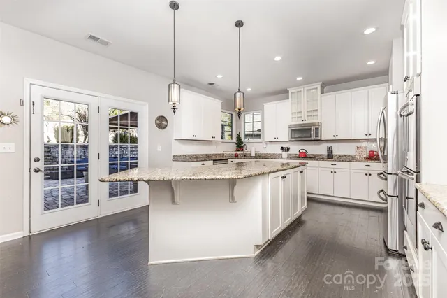 a kitchen with stainless steel appliances kitchen island granite countertop a stove a sink and white cabinets with wooden floor