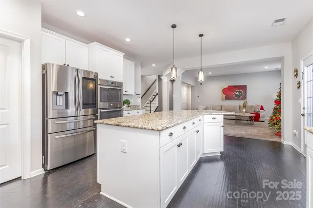 a kitchen with stainless steel appliances kitchen island granite countertop a refrigerator a stove and a wooden floors