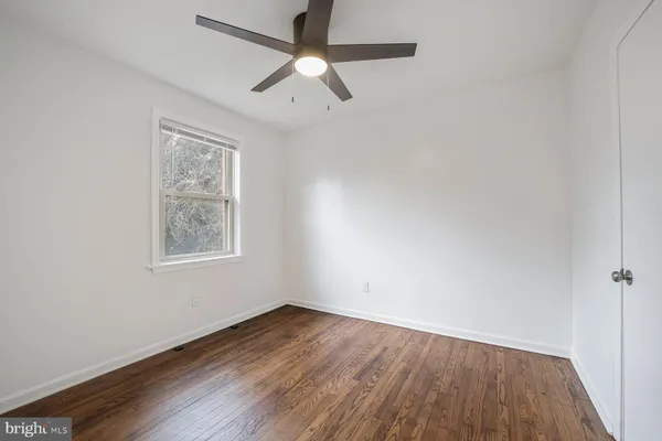 an empty room with wooden floor ceiling fan and windows