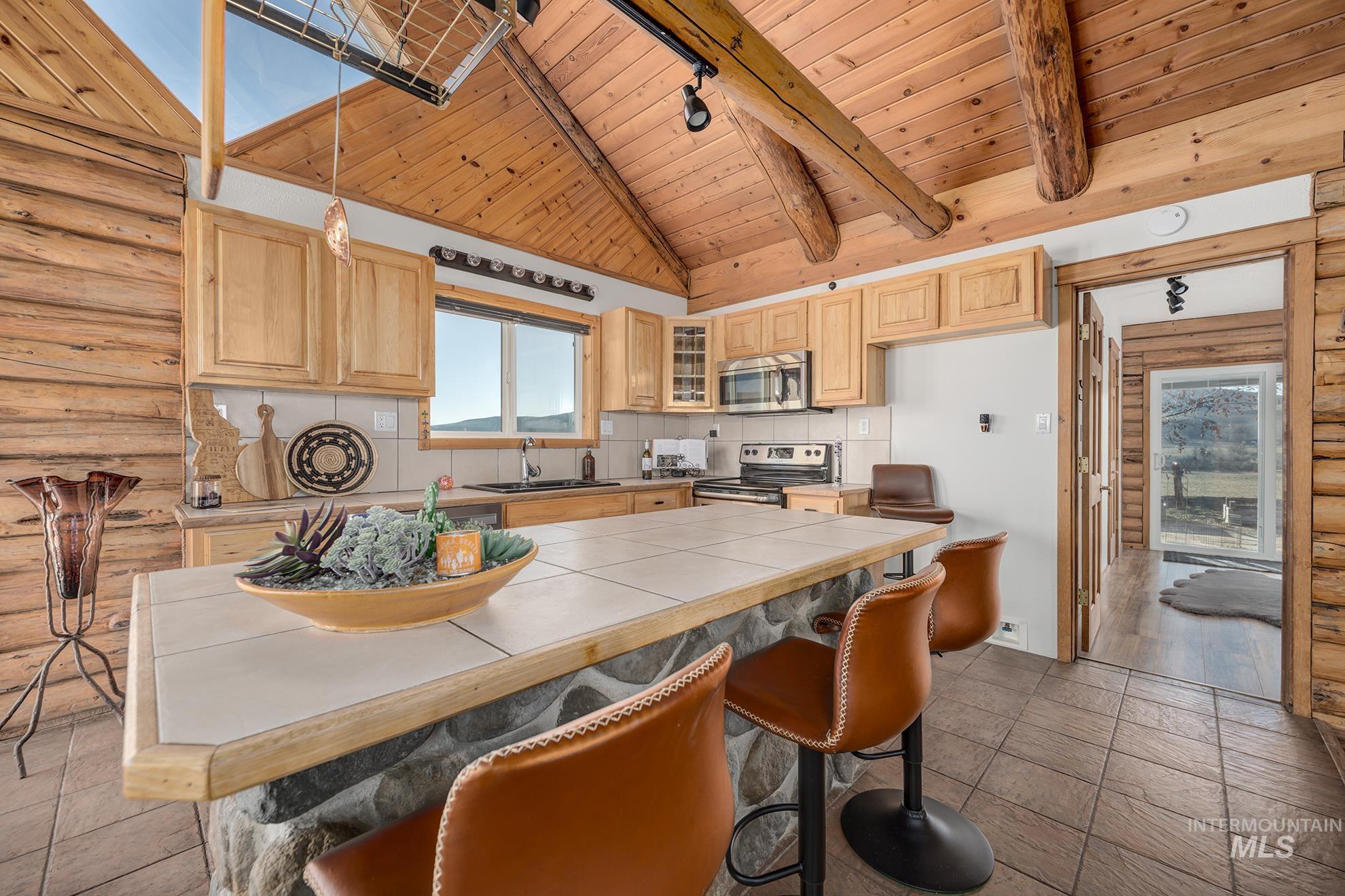 1855 Jones Road Weiser, ID 83672 - Photo 10 of 34 Kitchen featuring log walls, a high wooden beamed ceiling, a breakfast bar, light wood finish cabinetry, and plenty of natural light
