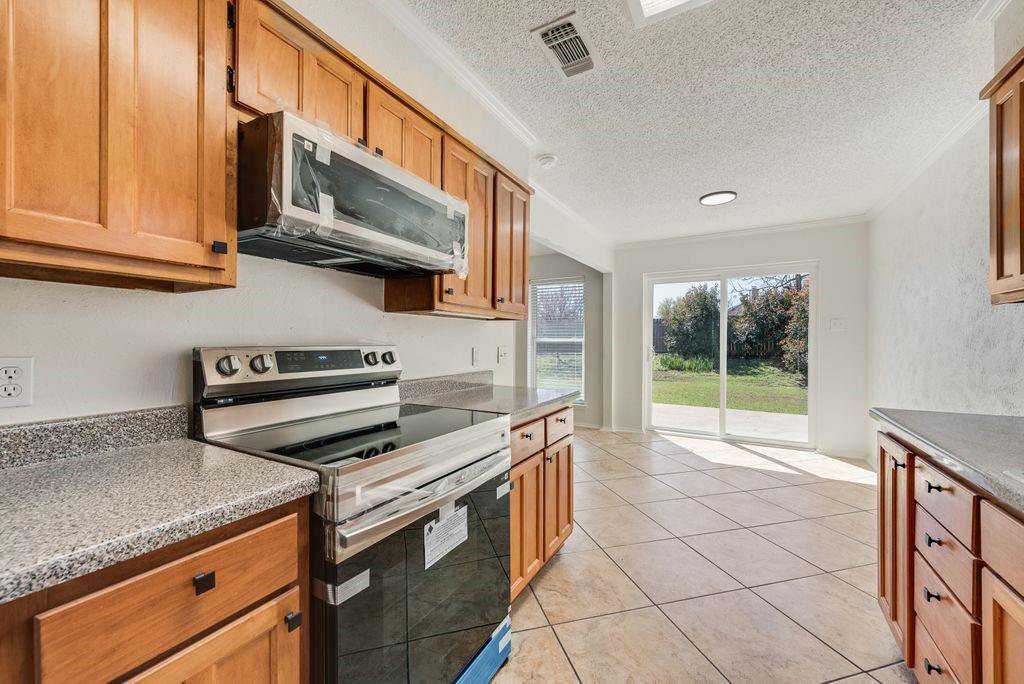 1532 Augusta Road Benbrook, TX 76126 - Photo 11 of 31 Kitchen with stainless steel appliances, a textured ceiling, light tile patterned flooring, wood finish cabinetry, and crown molding