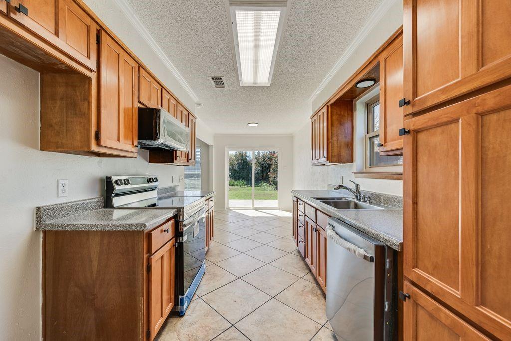1532 Augusta Road Benbrook, TX 76126 - Photo 12 of 31 Kitchen featuring stainless steel appliances, a textured ceiling, wood finish cabinets, light tile patterned floors, and crown molding