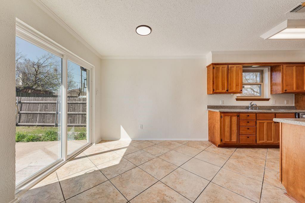 1532 Augusta Road Benbrook, TX 76126 - Photo 8 of 31 Kitchen with wood finish cabinetry, a textured ceiling, light countertops, light tile patterned floors, and crown molding
