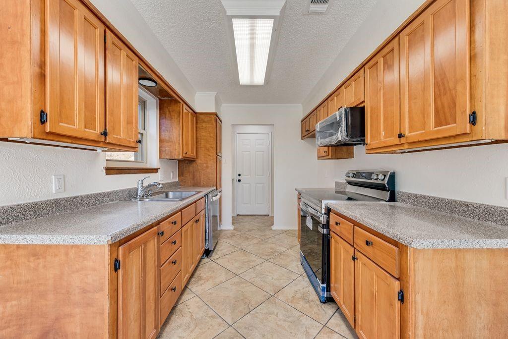 1532 Augusta Road Benbrook, TX 76126 - Photo 9 of 31 Kitchen featuring stainless steel appliances, a textured ceiling, wood finish cabinetry, light tile patterned flooring, and light stone counters