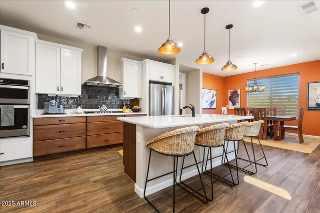 a kitchen with stainless steel appliances granite countertop a stove a refrigerator a oven a dining table and chairs with wooden floor