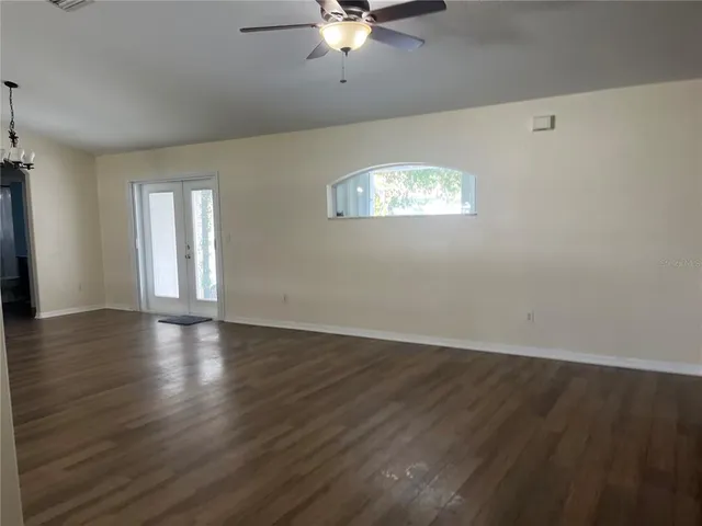 an empty room with wooden floor chandelier and windows