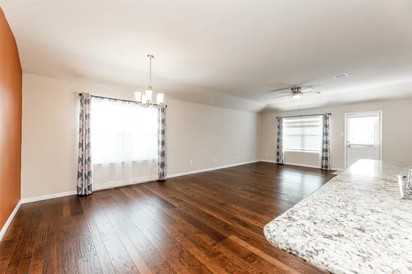 an empty room with wooden floor chandelier and windows