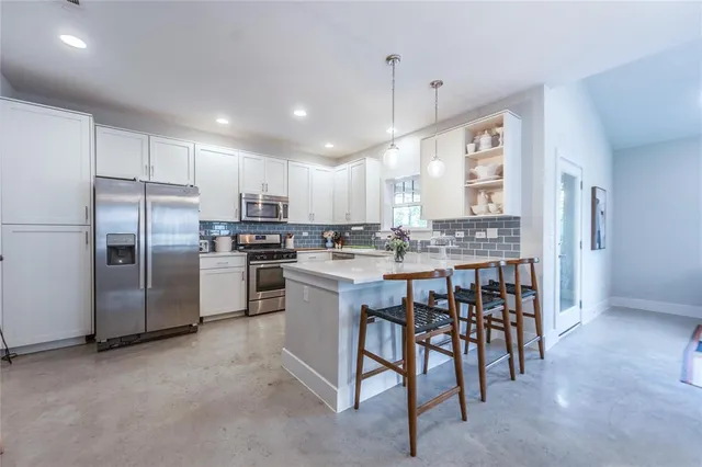 a kitchen with stainless steel appliances kitchen island granite countertop a refrigerator a stove a sink with a dining table and chairs