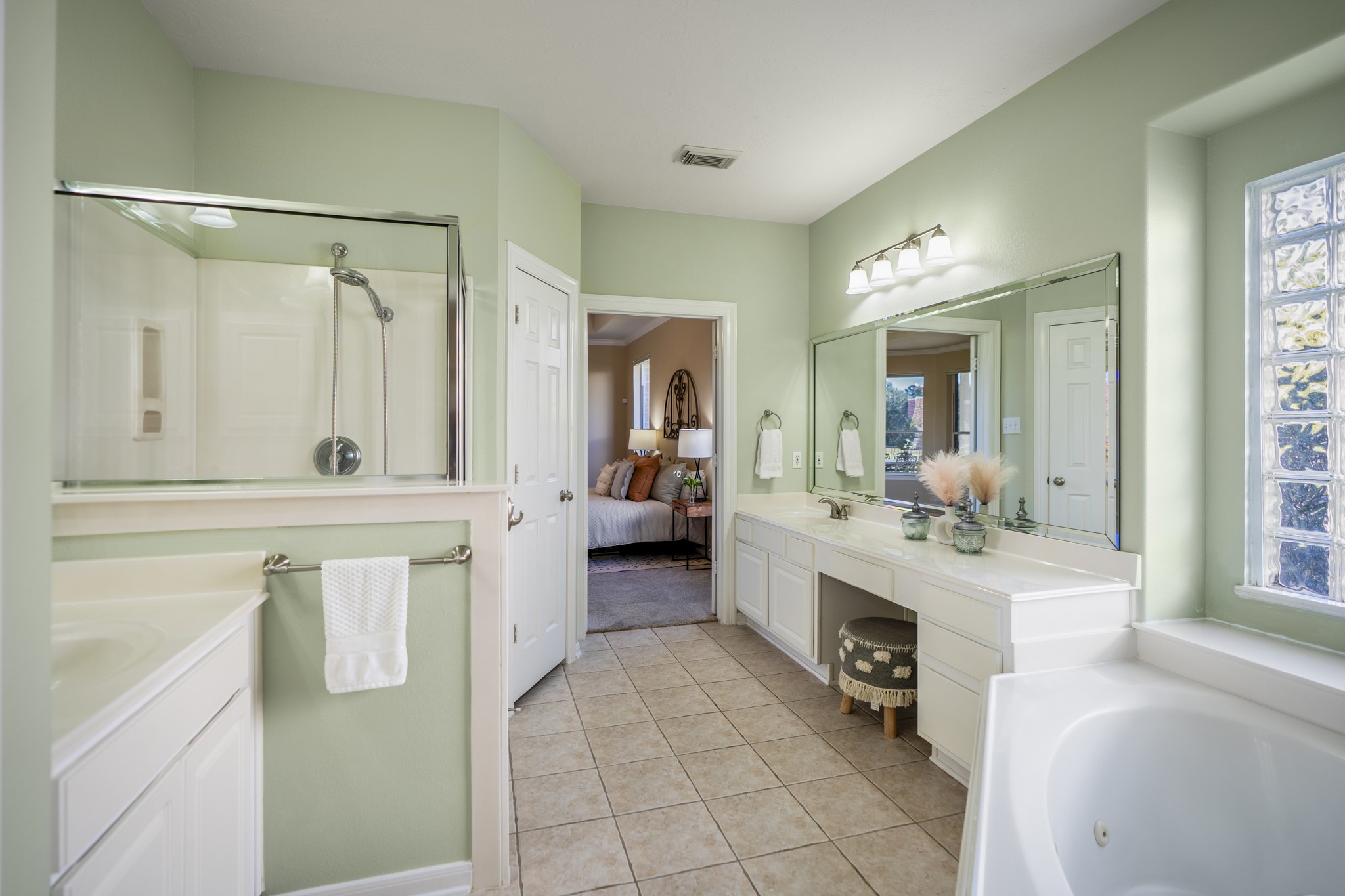 6218 Stone Trail Lane Spring, TX 77379 - Photo 20 of 50 The primary bathroom continues the calm, spa-like feel with a long vanity offering plenty of counter space, a seated makeup area, and wide mirrors that reflect natural light. A soaking tub, separate glass-enclosed shower, and soft green tones create a space designed for both everyday routines and unhurried mornings.