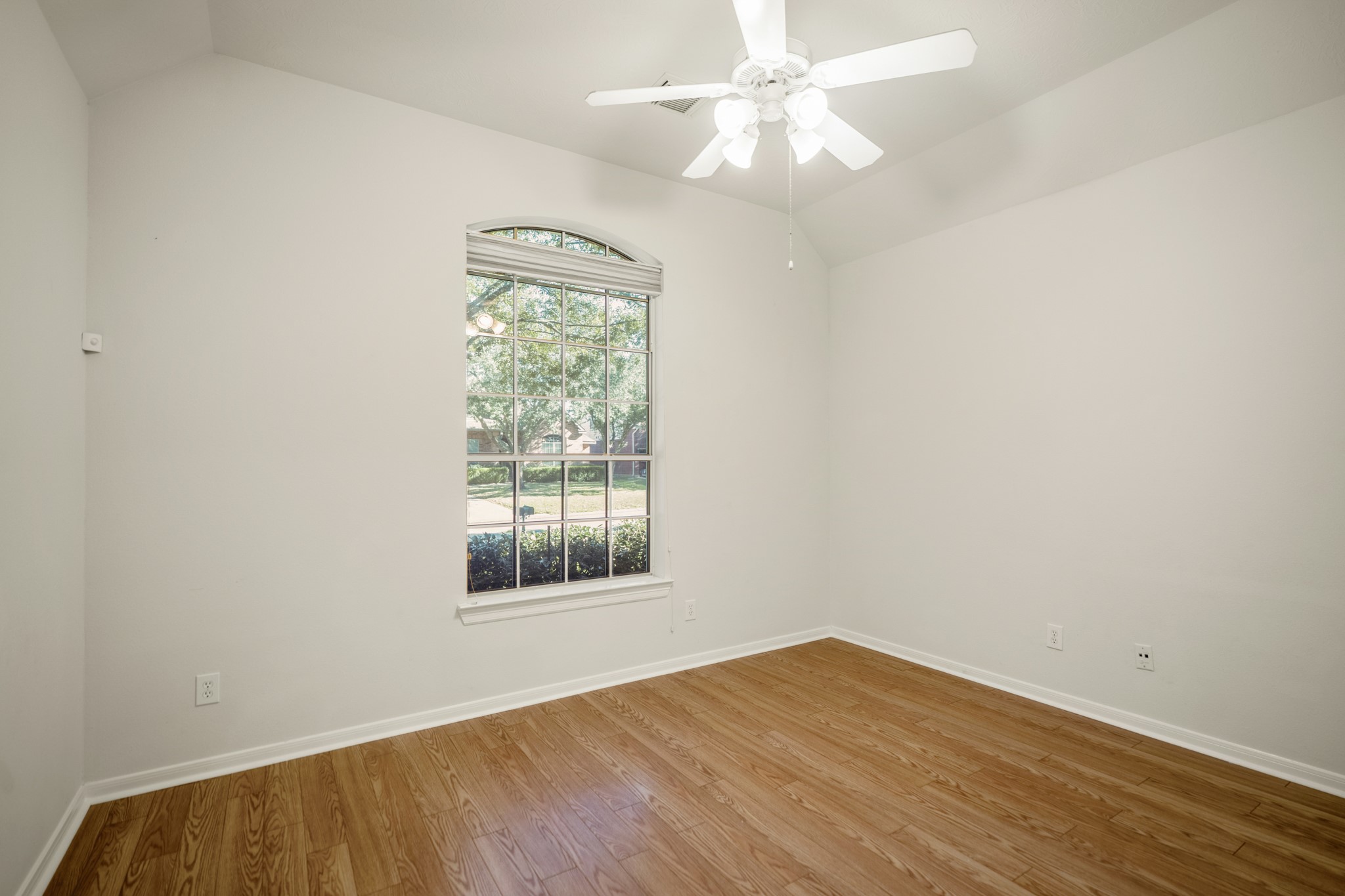 6218 Stone Trail Lane Spring, TX 77379 - Photo 22 of 50 Warm laminate flooring and a vaulted ceiling give this secondary bedroom an airy, open feel, while the arched window brings in soft natural light and leafy views outside.