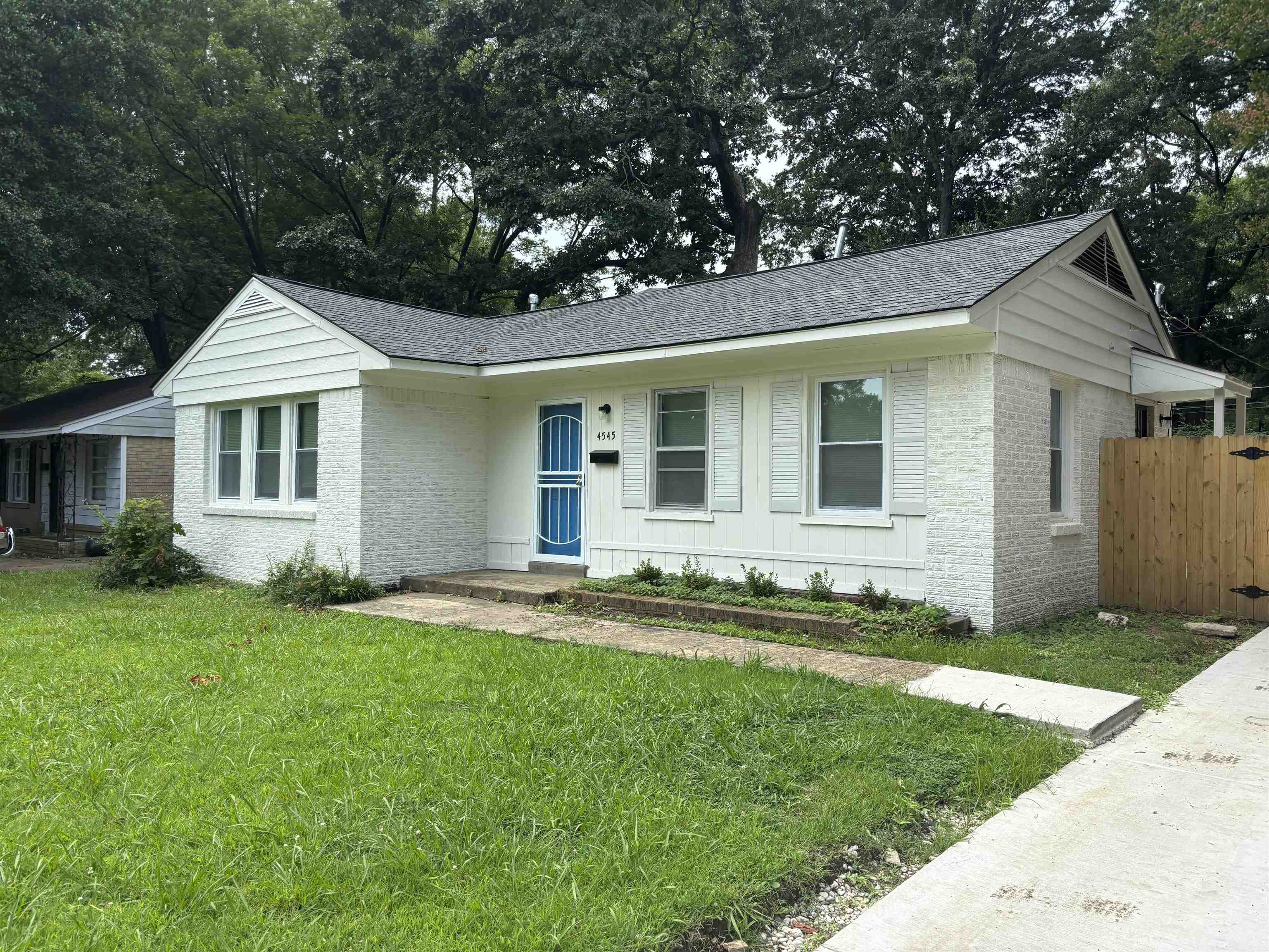 4545 Verne Road Memphis, TN 38117 - Photo 2 of 10 White brick exterior featuring a newly installed dark shingle roof and a vibrant blue security screen door