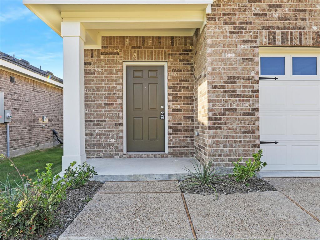 4510 Winecup Road Melissa, TX 75454 - Photo 3 of 22 Brick exterior featuring a covered front porch with a white column, a dark paneled entry door, and an attached garage with a white panel door