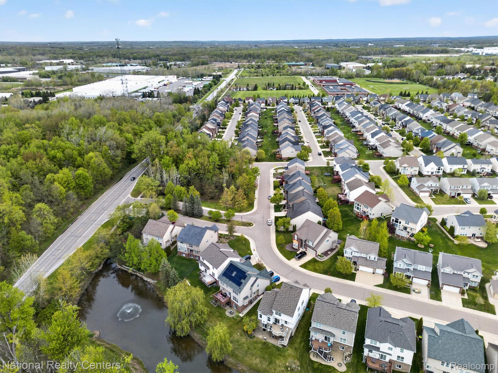 27412 Victoria Road Novi, MI 48374 - Photo 56 of 61 Aerial perspective of a residential neighborhood with diverse architectural styles, mature trees, a pond with a fountain, and paved roads