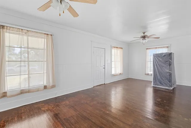 an empty room with wooden floor chandelier fan and windows