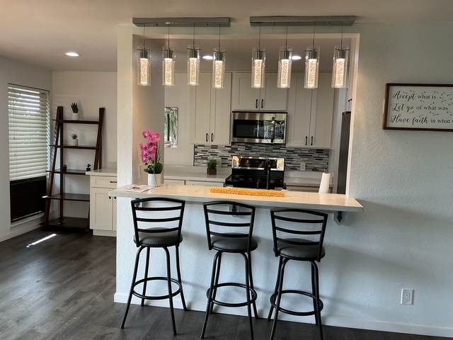 a kitchen with stainless steel appliances kitchen island granite countertop a dining table chairs and a refrigerator