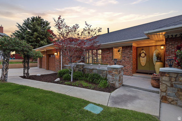 2342 Charros Road Sandy, UT 84092 - Photo 4 of 94 Brick exterior with stone accents, featuring a two-car garage with wood-finish doors, a concrete walkway, and landscaped garden beds