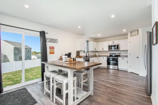 a view of a kitchen with kitchen island stainless steel appliances wooden floor dining table and chairs